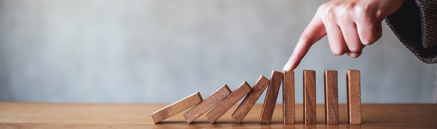 Ralf Baumhöfer – Psychotherapiepraxis – Dieses Bild ist eine Konzeptzeichnung: Ein Finger hält eine Kette fallender Dominosteine ​​aus Holz auf.